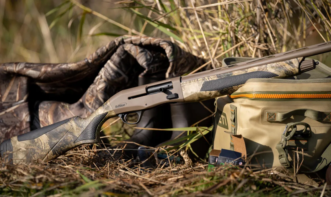 TriStar Viper G2 PRO in camo with a flat dark earth receiver and overmolded grips leaning on a blind bag in marsh grass, TriStar photo