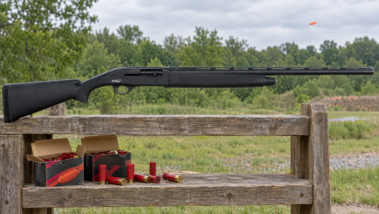 TriStar Viper G2 Synthetic shotgun resting on a wooden rack at a sporting clays station above open boxes of red target shotshells