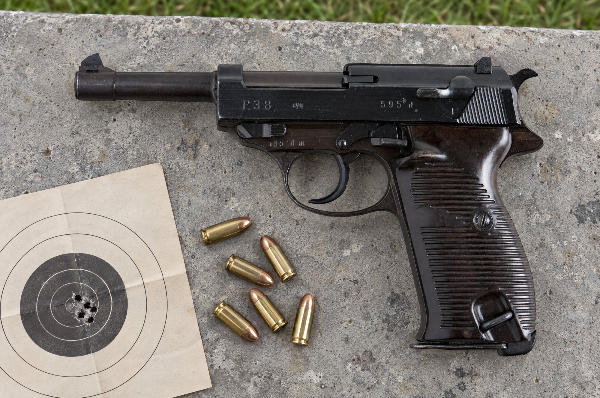 Walther P38 lying on a concrete range bench beside loose 9mm cartridges and a paper target