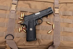 Wilson Combat CQB Elite Commander 1911 pistol on a tan range bag with loose cartridges