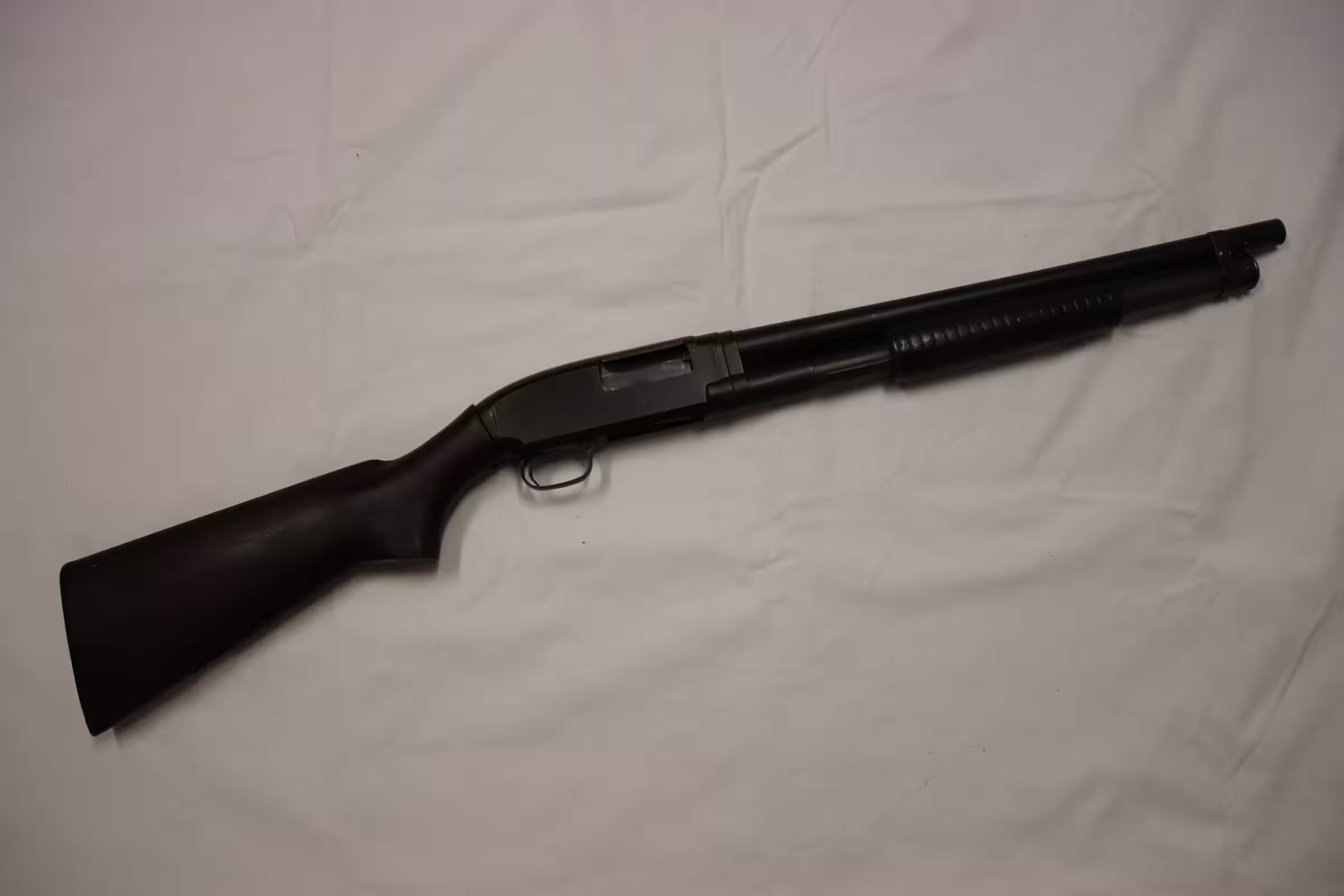 Winchester Model 12 riot shotgun with U.S. marked receiver, short plain barrel and walnut stock on a white cloth