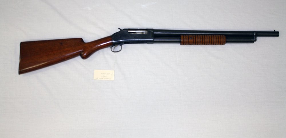 Winchester Model 1897 riot shotgun with short plain barrel and exposed hammer, right side on white cloth
