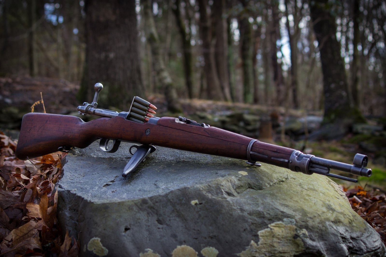 Yugoslavian M24/47 Mauser rifle on a mossy rock with a stripper clip of 8mm Mauser cartridges and an M48 bayonet