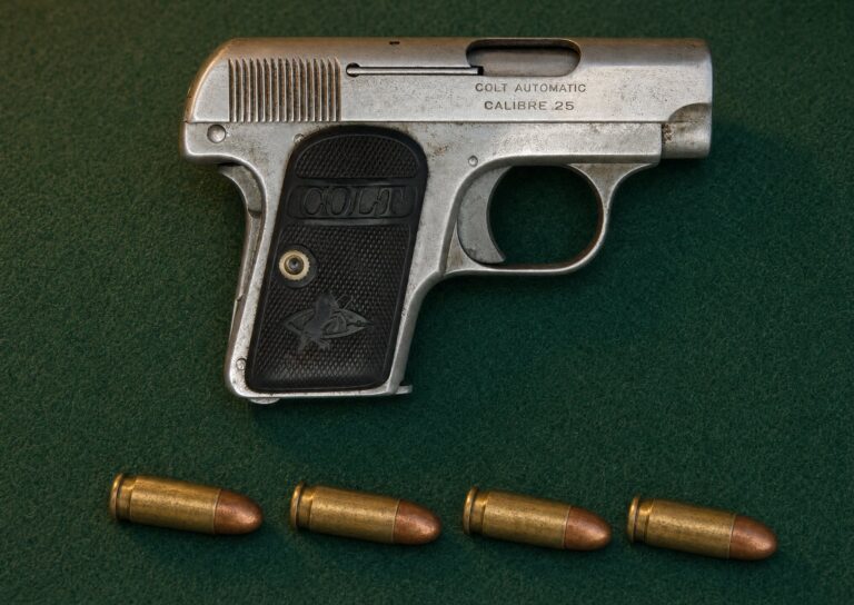 Four 25 ACP cartridges on green felt beside a nickel Colt 1908 Vest Pocket pistol marked Calibre .25
