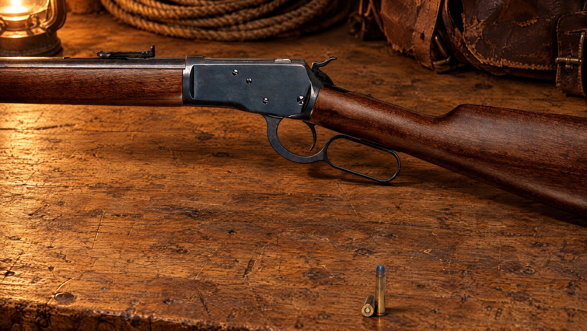 Two 32-20 ammo cartridges on a workbench in front of a Winchester Model 1892 lever-action rifle