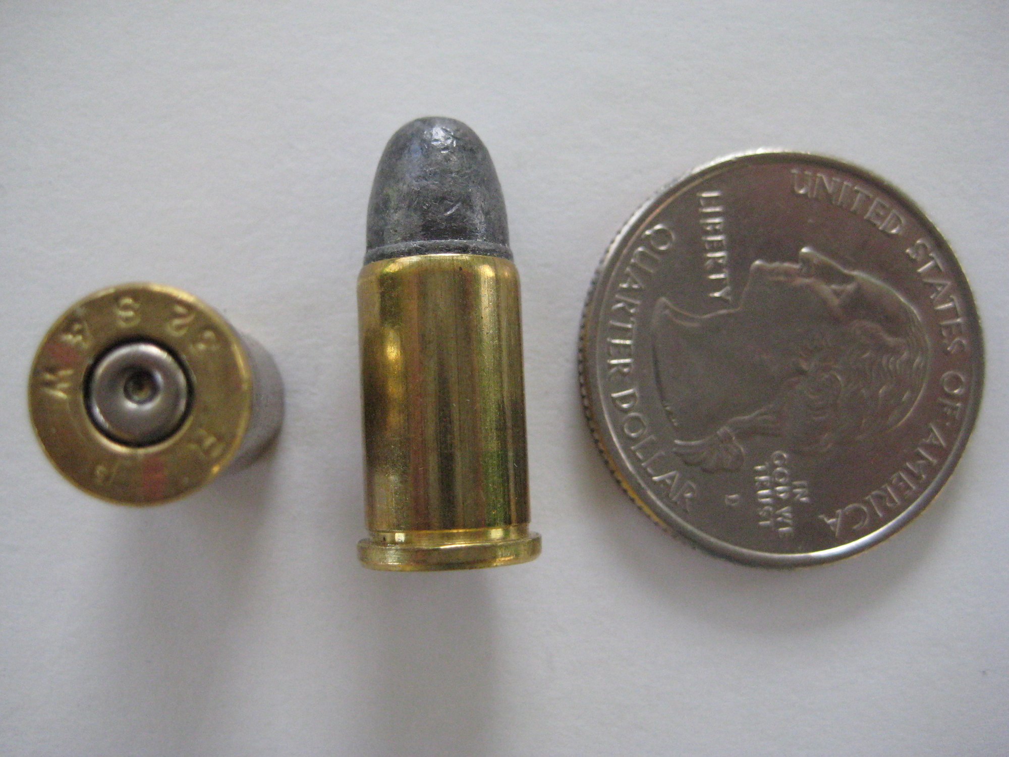 32 S&W cartridge and empty case showing its headstamp beside a quarter