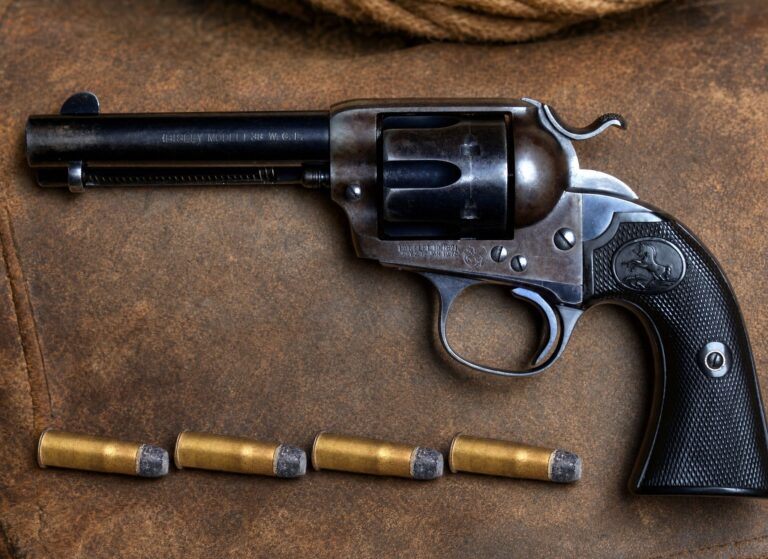 Four 38-40 cartridges on a leather saddlebag beside a Colt Bisley revolver marked 38 W.C.F.