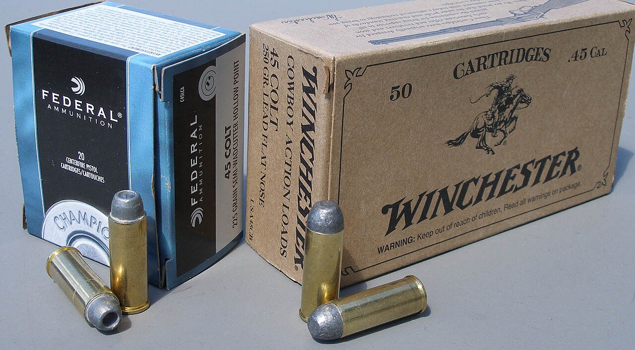Federal and Winchester boxes of 45 Colt ammo with two cartridges in front of each