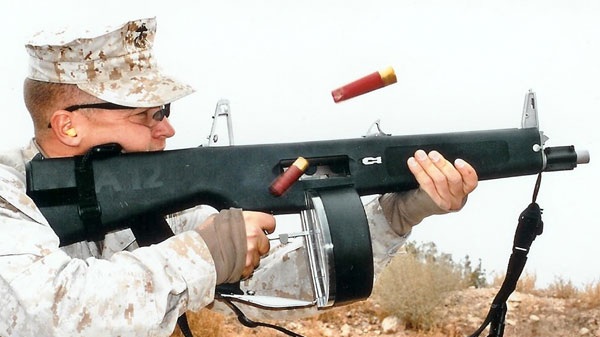 Marine firing a drum-fed AA-12 full-auto combat shotgun, shotshells ejecting in the air