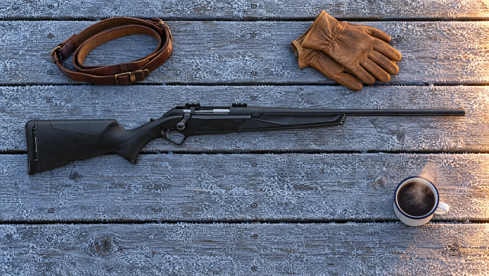 Benelli Lupo rifle lying flat on frosty wooden deck boards at dawn beside a leather sling, gloves and a camp mug