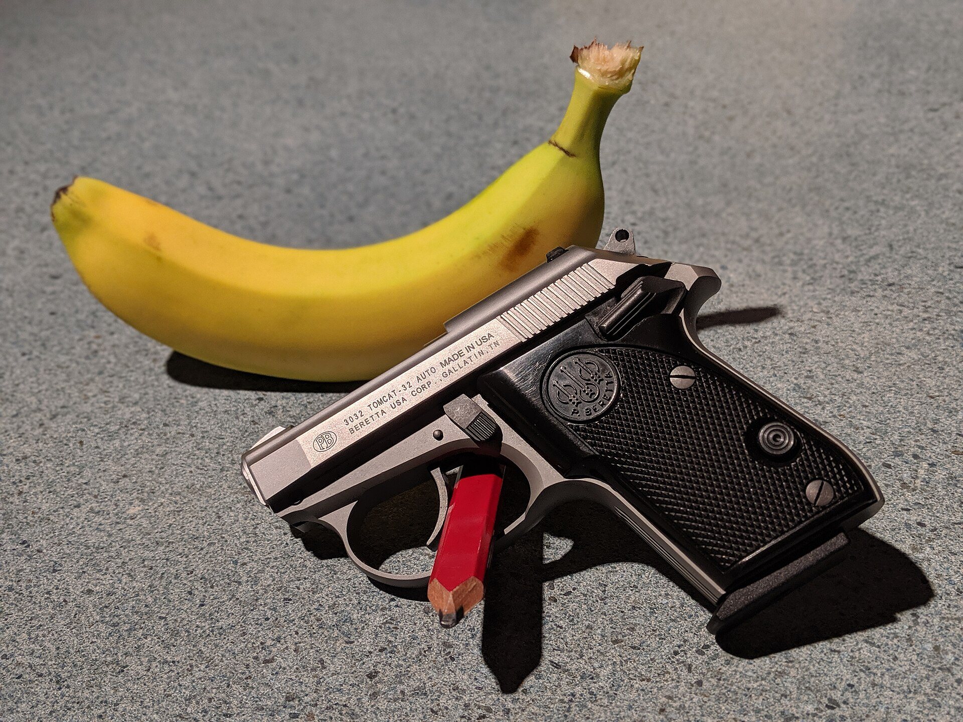 Stainless Beretta 3032 Tomcat pistol in 32 ACP beside a banana for scale