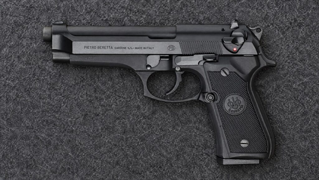 Beretta 92FS left side lying flat on a gray blanket, showing the slide-mounted safety lever, slide stop and takedown lever