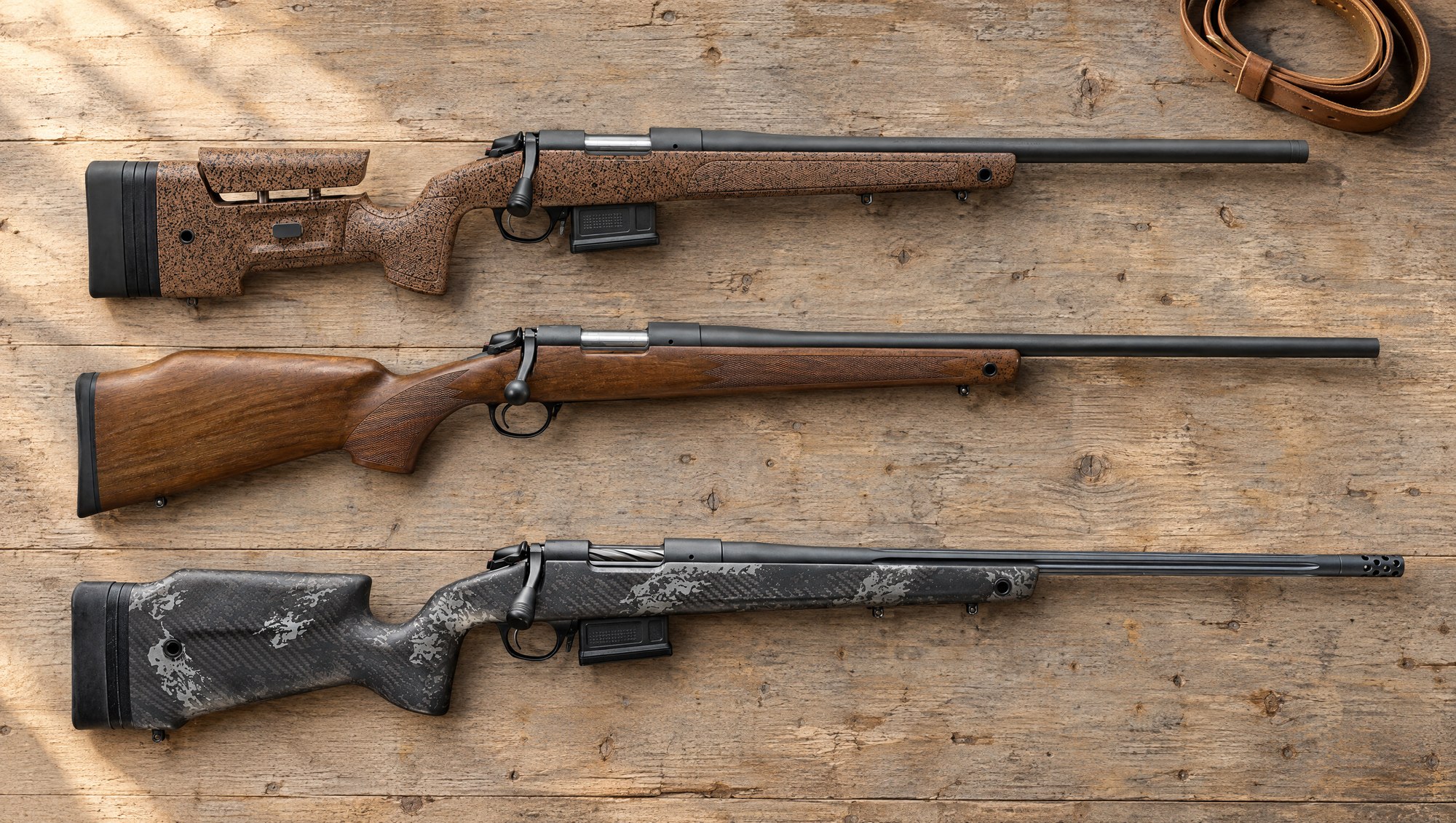 Bergara B-14 models compared: a B-14 HMR, a walnut B-14 Timber and a carbon-stocked B-14 Squared Crest lying flat on an oak workbench