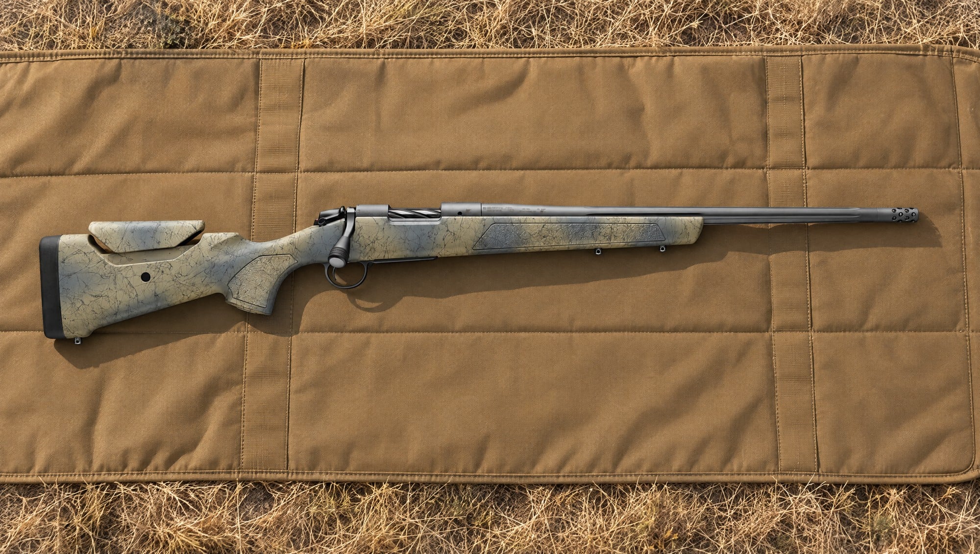 Bergara B-14 Wilderness Sierra with camo stock, fluted barrel and muzzle brake lying flat on a tan shooting mat on dry prairie grass