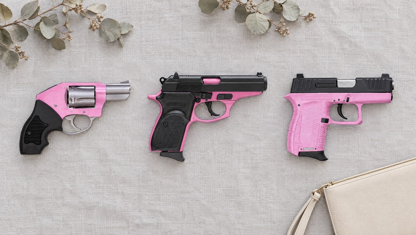 Three pink handguns lying flat on grey linen: a Charter Arms Pink Lady revolver, a Bersa Thunder 380 with a pink frame and a pink Diamondback DB380