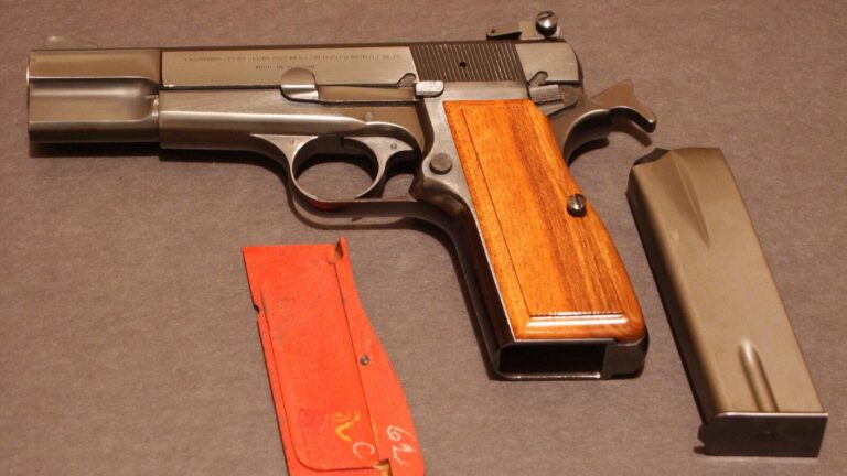A 1971 Belgian-made Browning Hi Power pistol with walnut grips, its magazine and a spare grip panel on a gray cloth