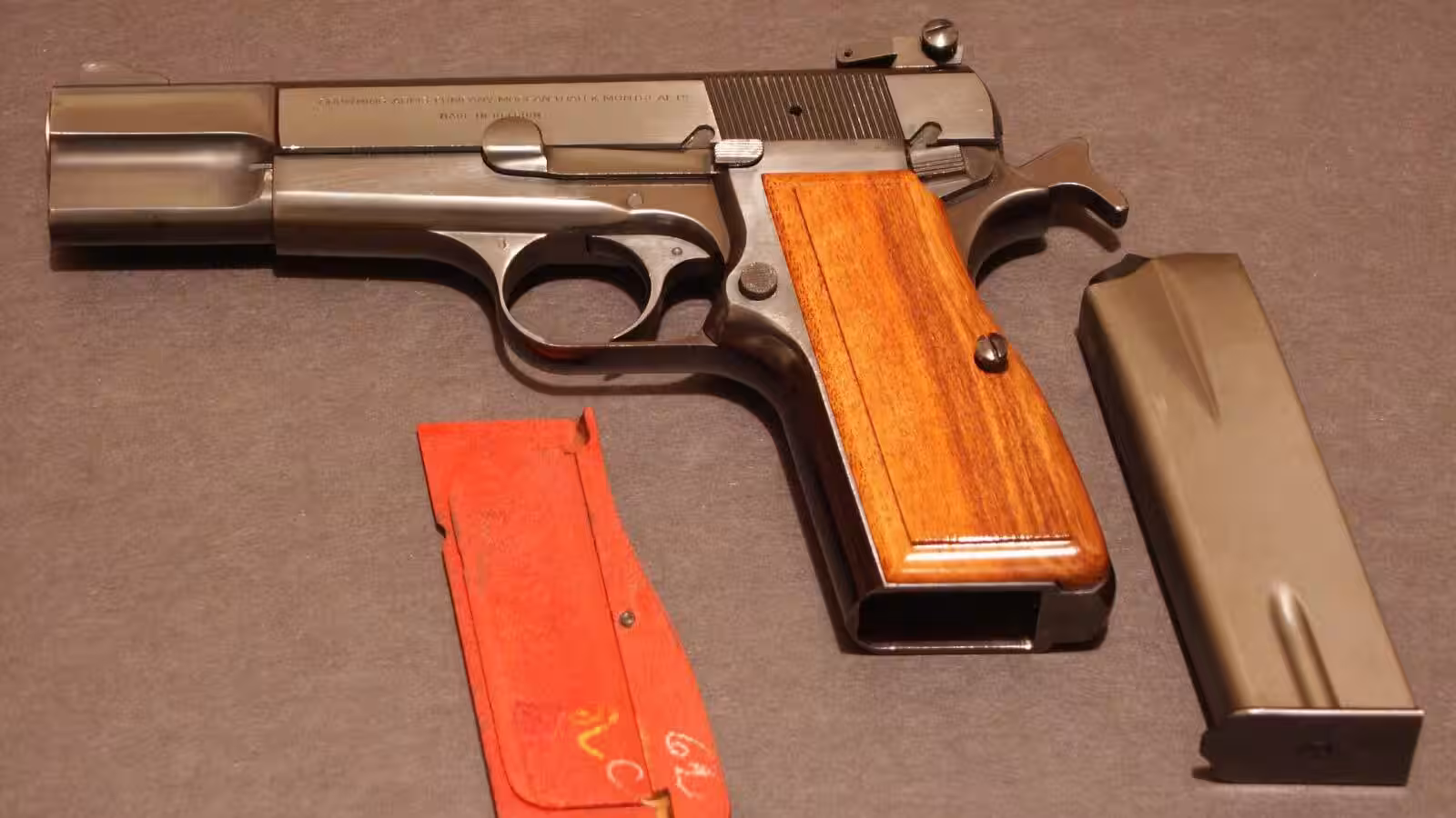 A 1971 Belgian-made Browning Hi Power pistol with walnut grips, its magazine and a spare grip panel on a gray cloth