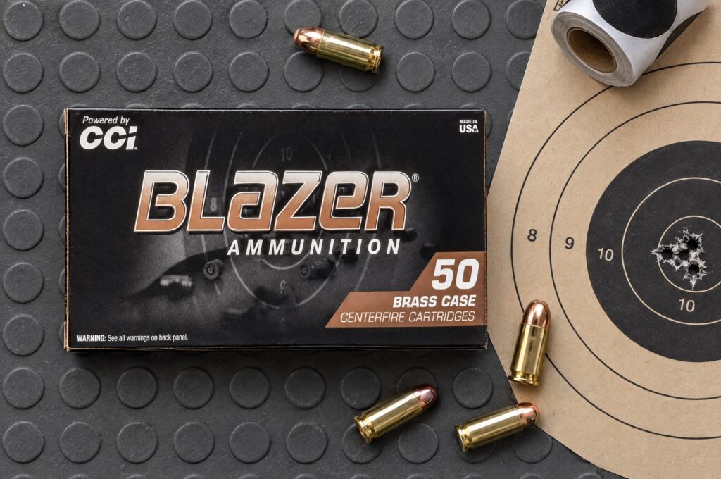 Box of CCI Blazer Brass 380 Auto 95 gr FMJ on a range mat beside a paper target with a tight group