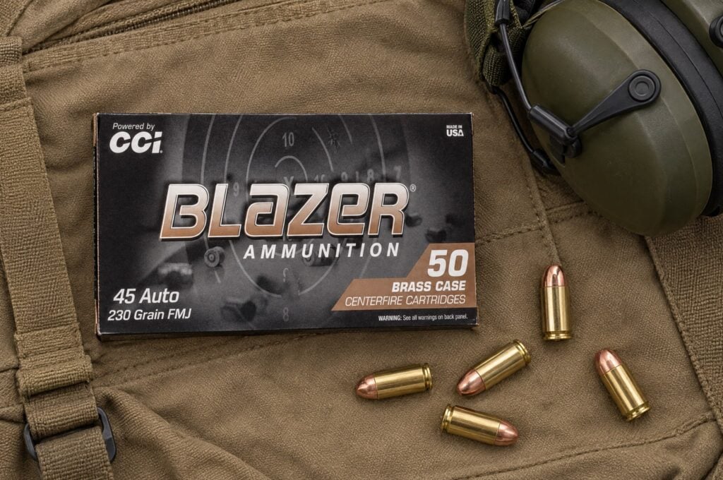 Box of CCI Blazer Brass 45 Auto 230 grain FMJ on a canvas range bag beside ear muffs and loose cartridges