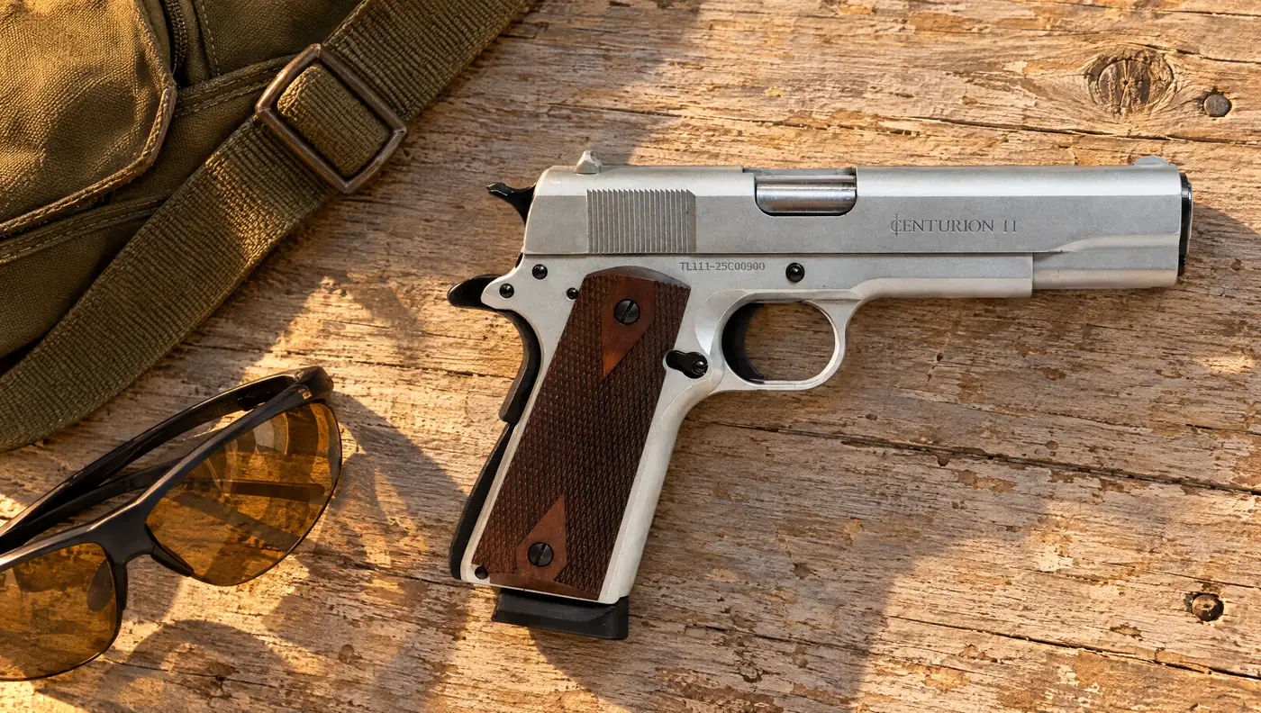 Chrome Century Arms Centurion 11 1911 with checkered wood grips lying on a weathered barn wood table beside shooting glasses and a canvas range bag