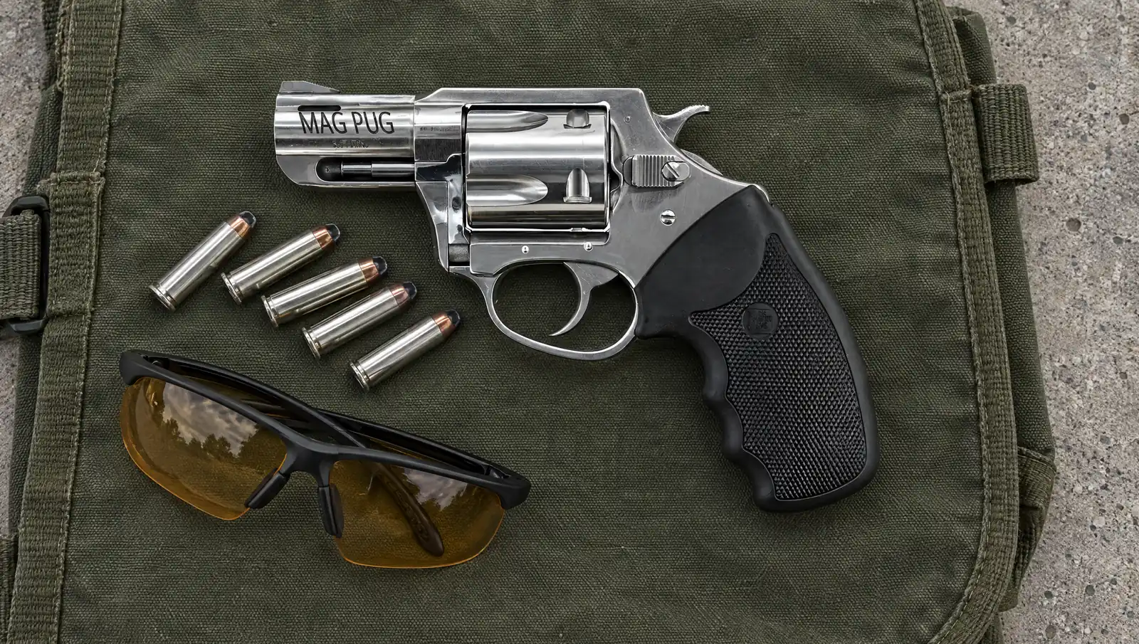 Charter Arms Mag Pug 73520 .357 Magnum revolver in polished stainless with a ported 2.2 inch barrel marked MAG PUG and a black rubber grip, lying on a canvas range bag beside five .357 Magnum cartridges and shooting glasses