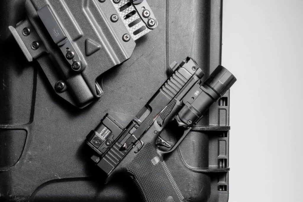 Pistol with a red dot and a Cloud Defensive EPL light lying on a hard case beside a light-bearing holster