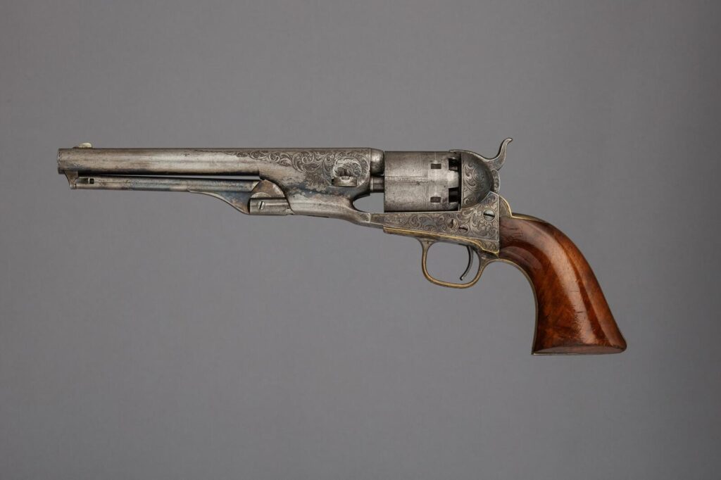 An engraved Colt Model 1861 Navy percussion revolver with a brass trigger guard and walnut grip, serial number 12240, on a gray background