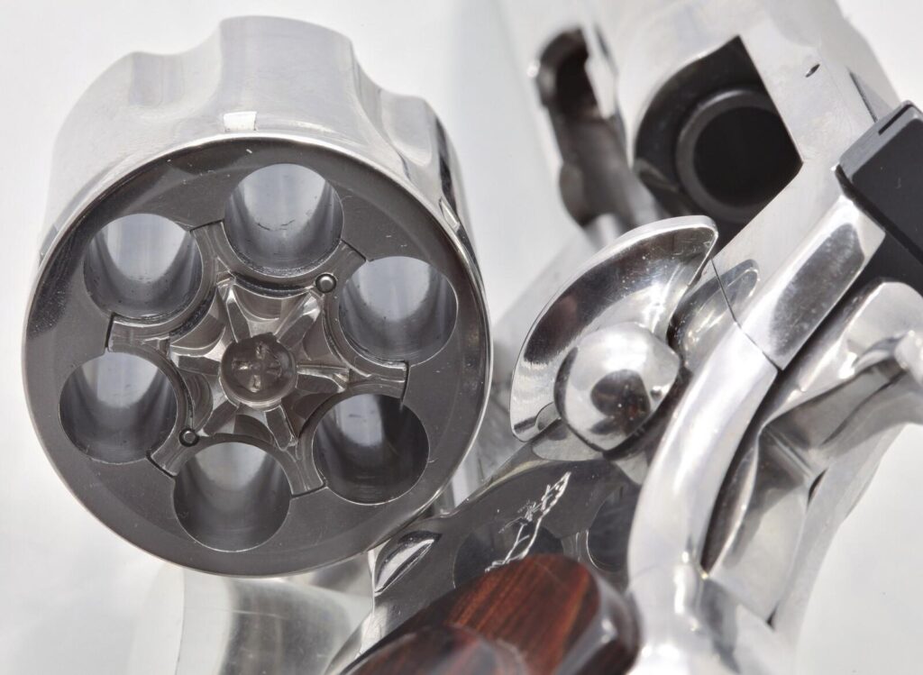 Close view of a Colt Python with the cylinder swung open, showing six chambers, the ejector star and the hammer