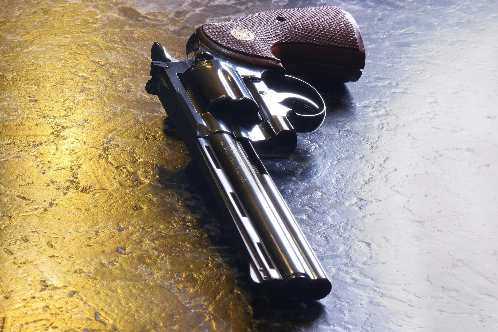 An original Colt Python with a six inch barrel, polished blue finish and fully checkered walnut grips lying on a textured gold and gray surface