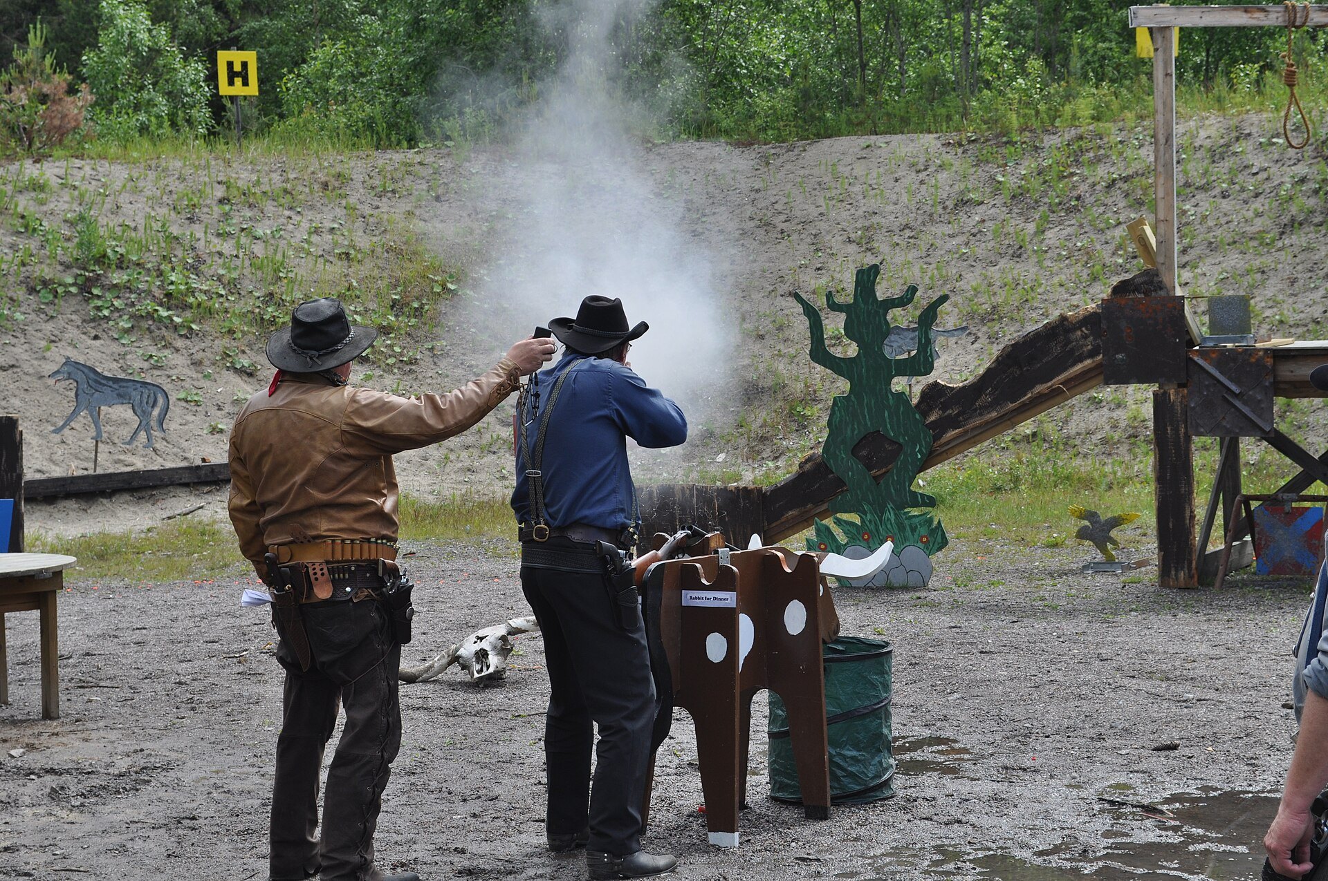Cowboy action shooter firing downrange through a cloud of smoke with a single action revolver holstered on his belt