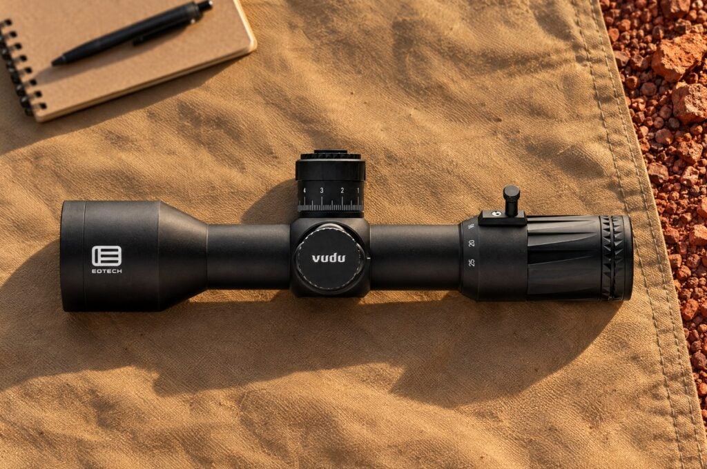 EOTech Vudu 5-25 power rifle scope lying on a tan shooting mat over red gravel
