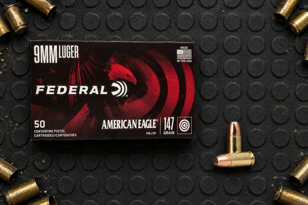 Federal American Eagle 9mm Luger 147 grain FMJ flat point box and cartridges on a rubber range mat ringed with spent brass