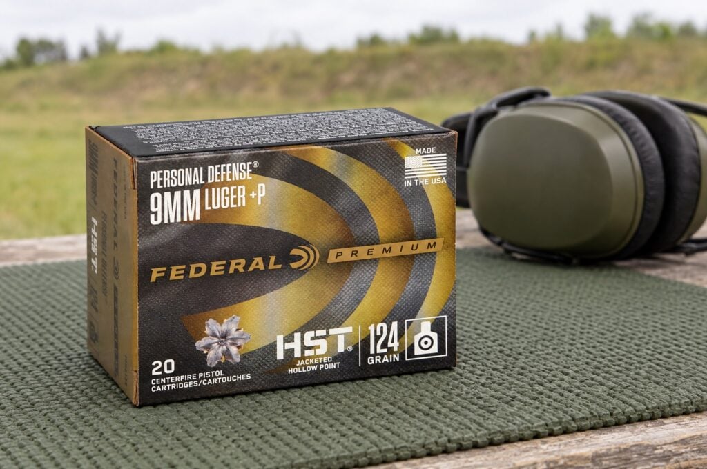 Personal Defense HST 9mm Luger +P 124 grain box on a shooting mat at an outdoor range beside ear muffs