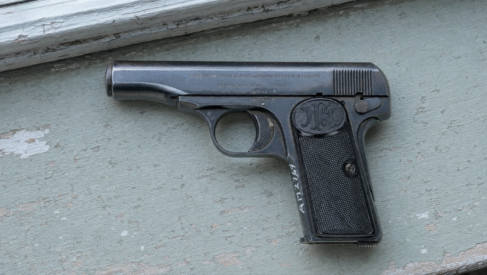 Blued FN Browning Model 1910 pistol in 7.65 mm on a gray-green painted windowsill
