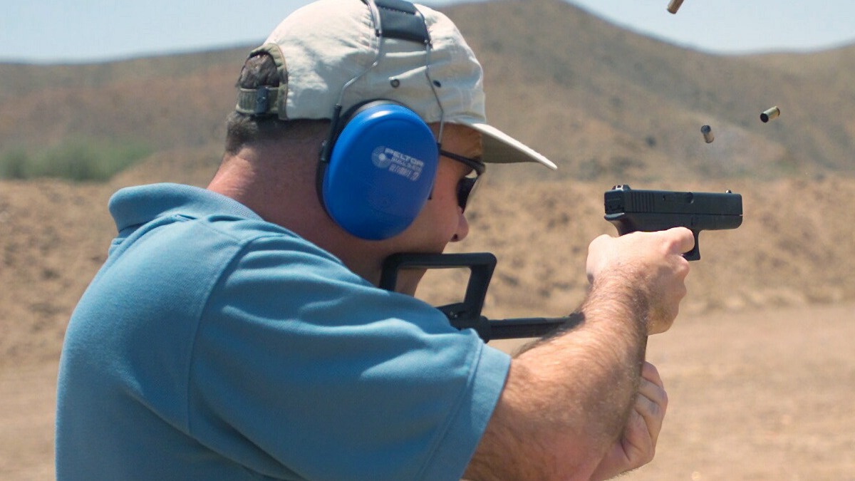 Shooter firing a Glock 18 machine pistol with a shoulder stock on full auto, spent brass in the air