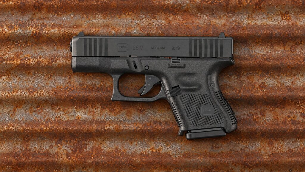 Black Glock 26 V subcompact pistol lying on rusted corrugated steel at dusk