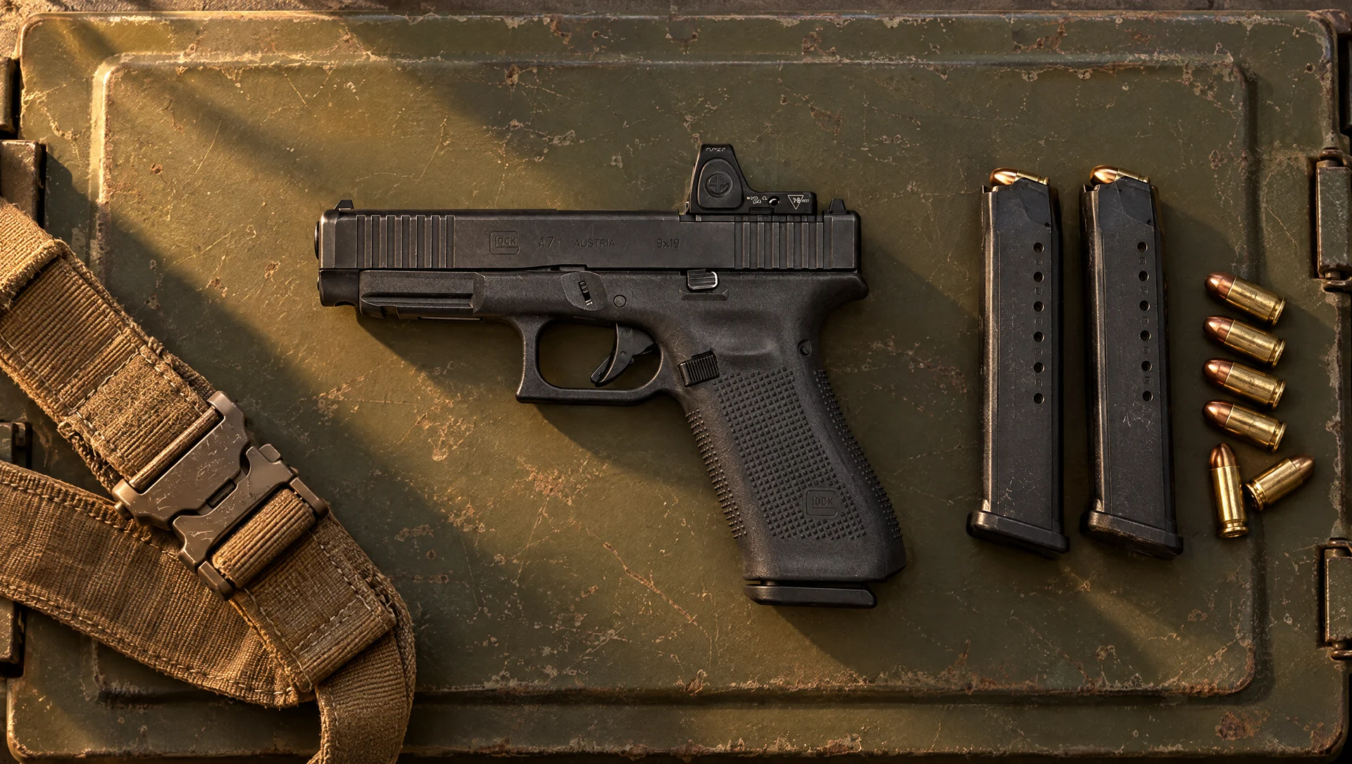 Glock 47 MOS 9mm with a red dot lying flat on an olive ammo can lid beside two magazines and 9mm cartridges