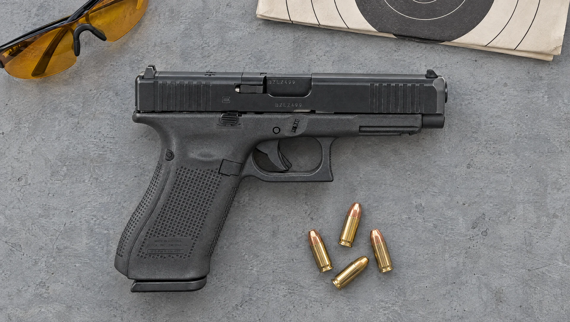 Right side of a Glock 47 MOS 9mm lying flat on a grey concrete range bench with shooting glasses and cartridges