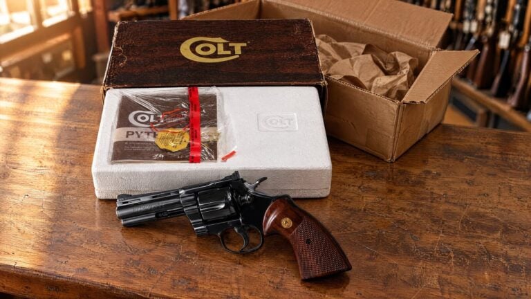 Blued four inch Colt Python lying on a gun shop counter beside its original Colt box and an opened shipping carton