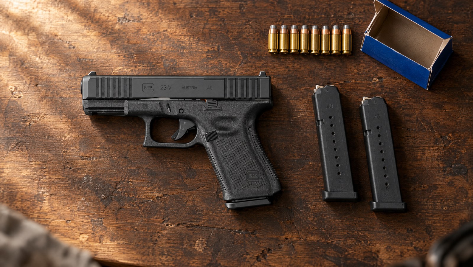 Glock 23 V .40 S&W pistol lying flat on a walnut bench beside two magazines and a row of .40 cartridges