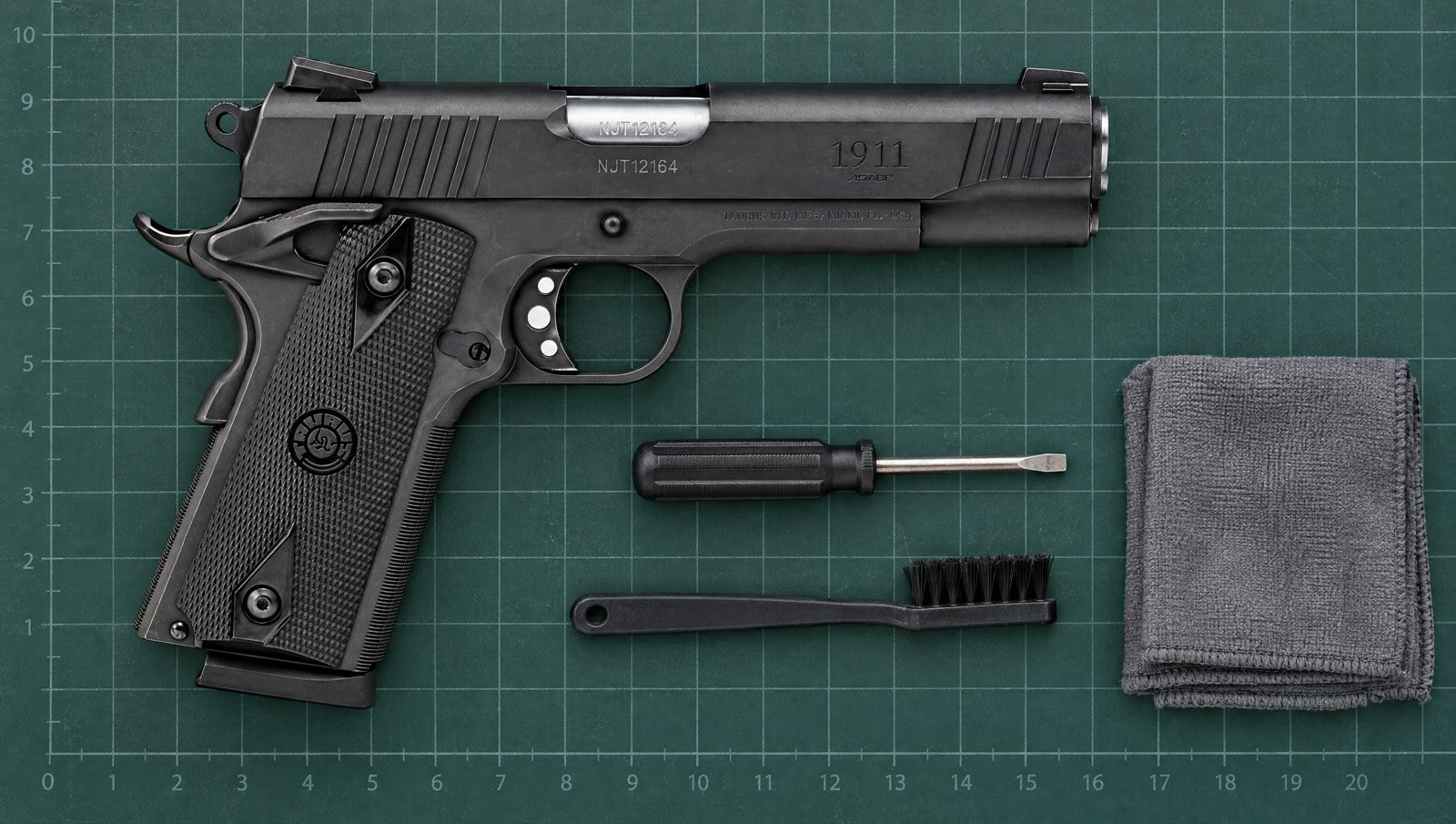 Taurus 1911 .45 ACP pistol on a green gunsmith mat beside a screwdriver, cleaning brush and cloth