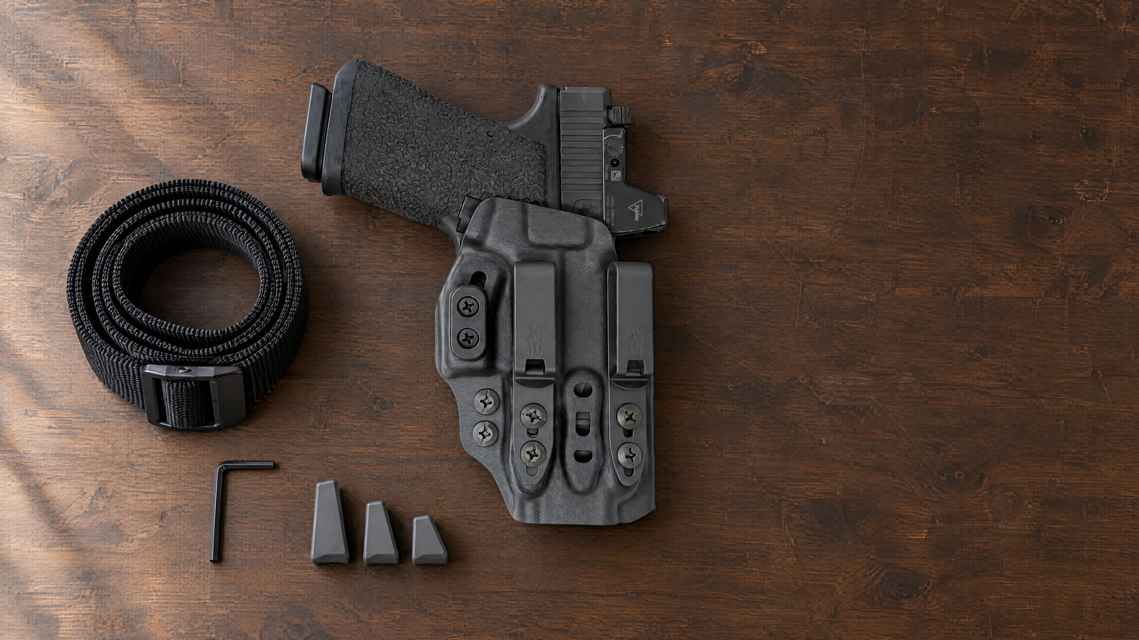 Tenicor VELO5 appendix holster with pistol lying flat on a walnut workbench beside a gun belt, hex key and three camming bars