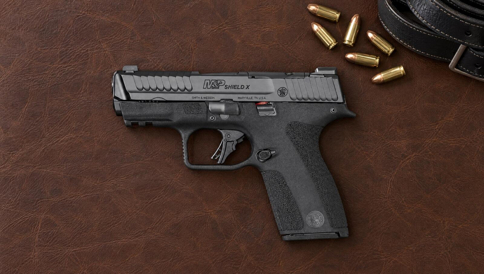 Smith and Wesson M&P Shield X 9mm pistol lying flat on a dark leather surface beside 9mm cartridges