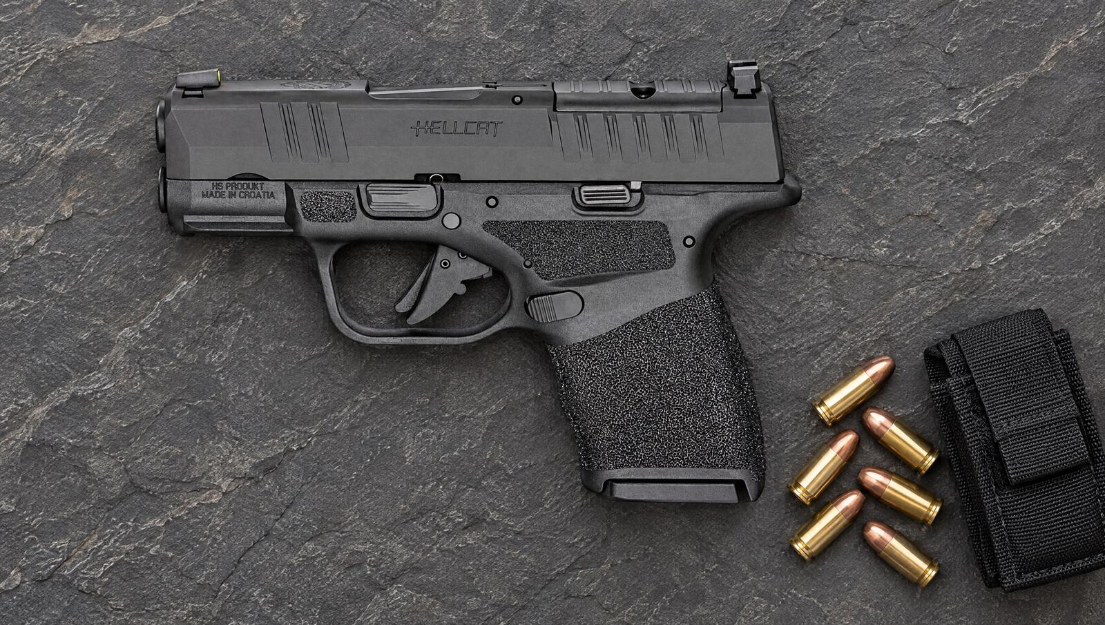 Springfield Armory Hellcat OSP 9mm micro-compact pistol lying flat on a slate surface beside 9mm cartridges