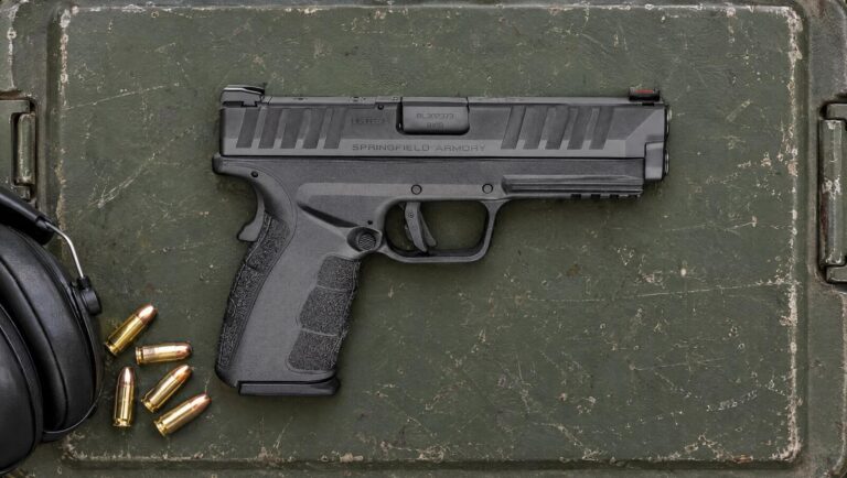 Springfield Armory XD Mod.4 OSP 9mm pistol lying flat on a green steel ammunition can lid beside 9mm cartridges and ear muffs