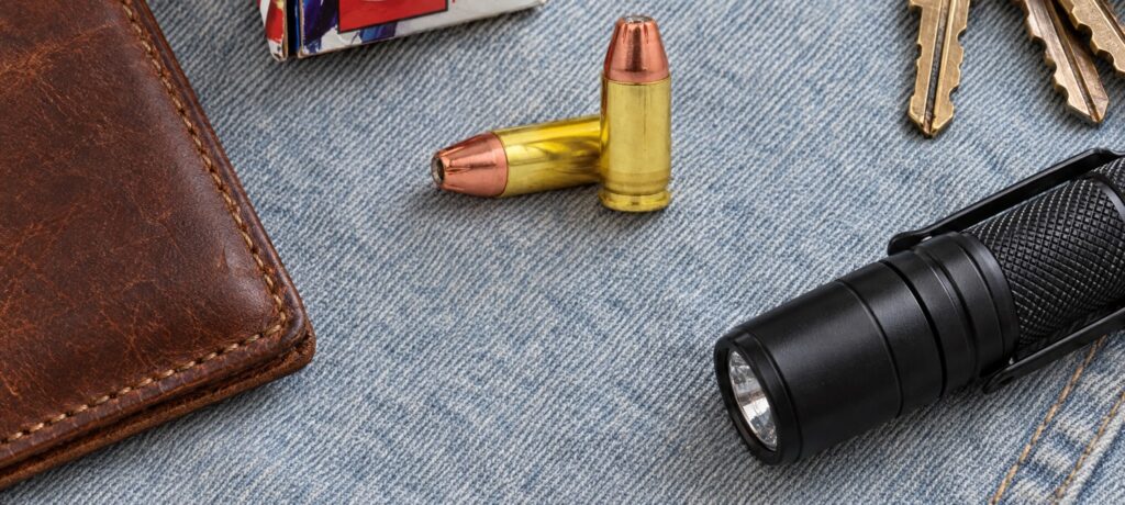 Two Hornady American Gunner 9mm Luger 115 gr XTP cartridges on denim beside a wallet, keys and a flashlight