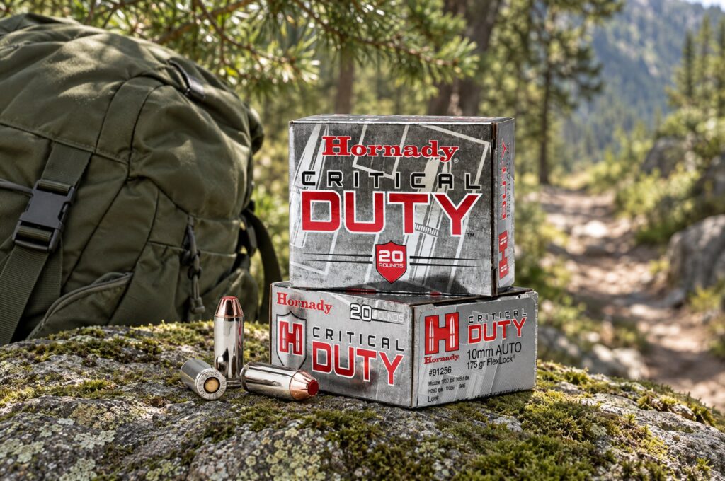 Two Hornady Critical Duty 10mm Auto 175 gr FlexLock boxes and three cartridges on mossy granite beside a hiking pack