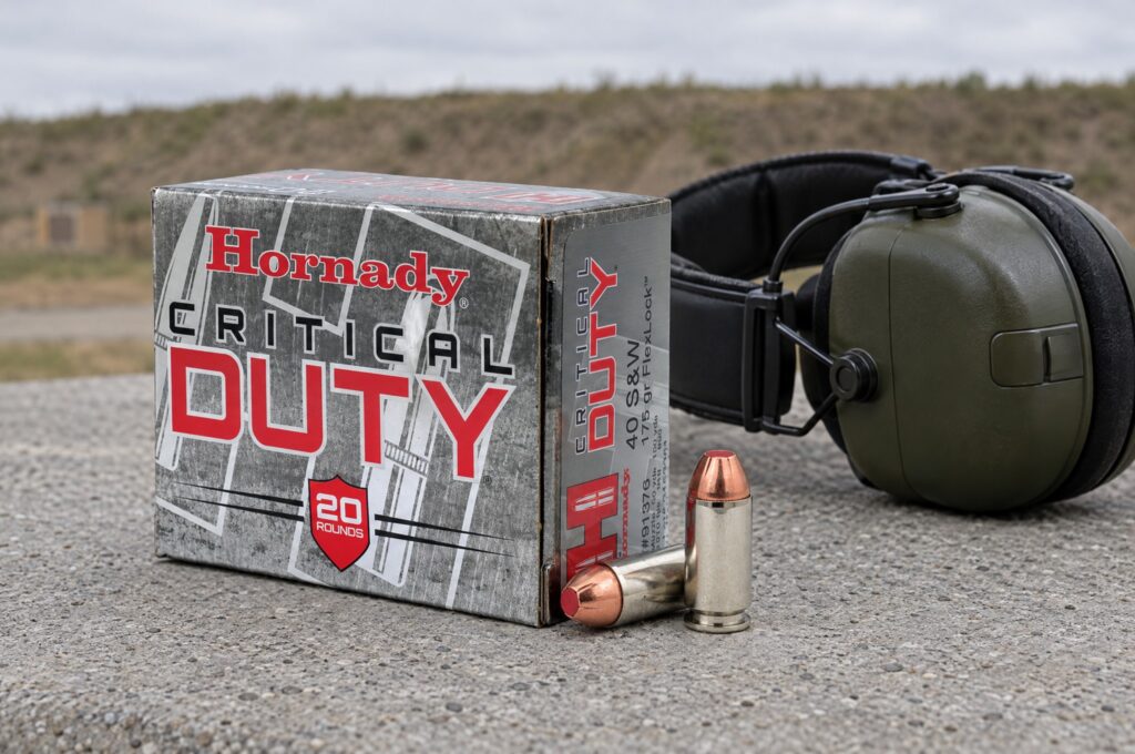 Hornady Critical Duty 40 S&W 175 gr FlexLock box and two cartridges on a concrete range bench beside ear muffs