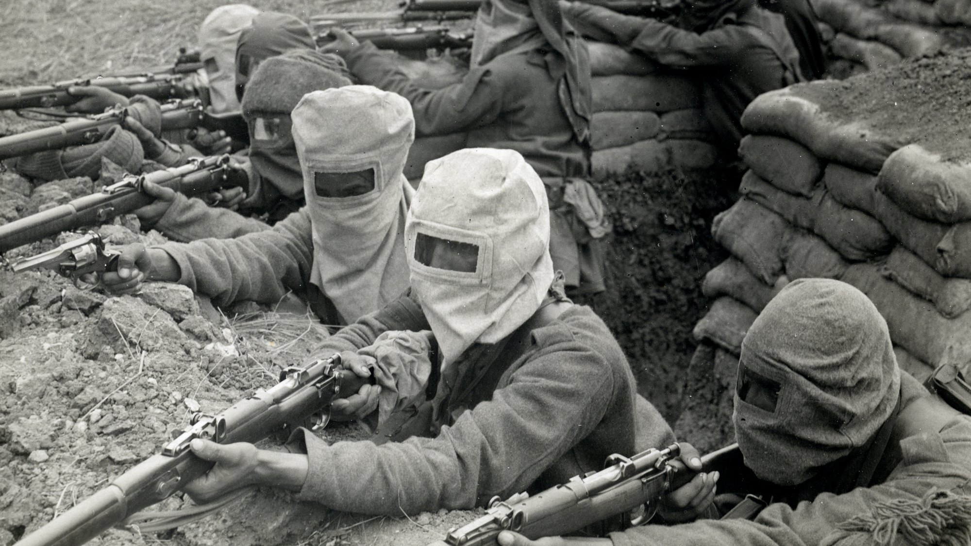Indian soldiers in gas hoods aiming Lee-Enfield rifles from a trench in France in 1915