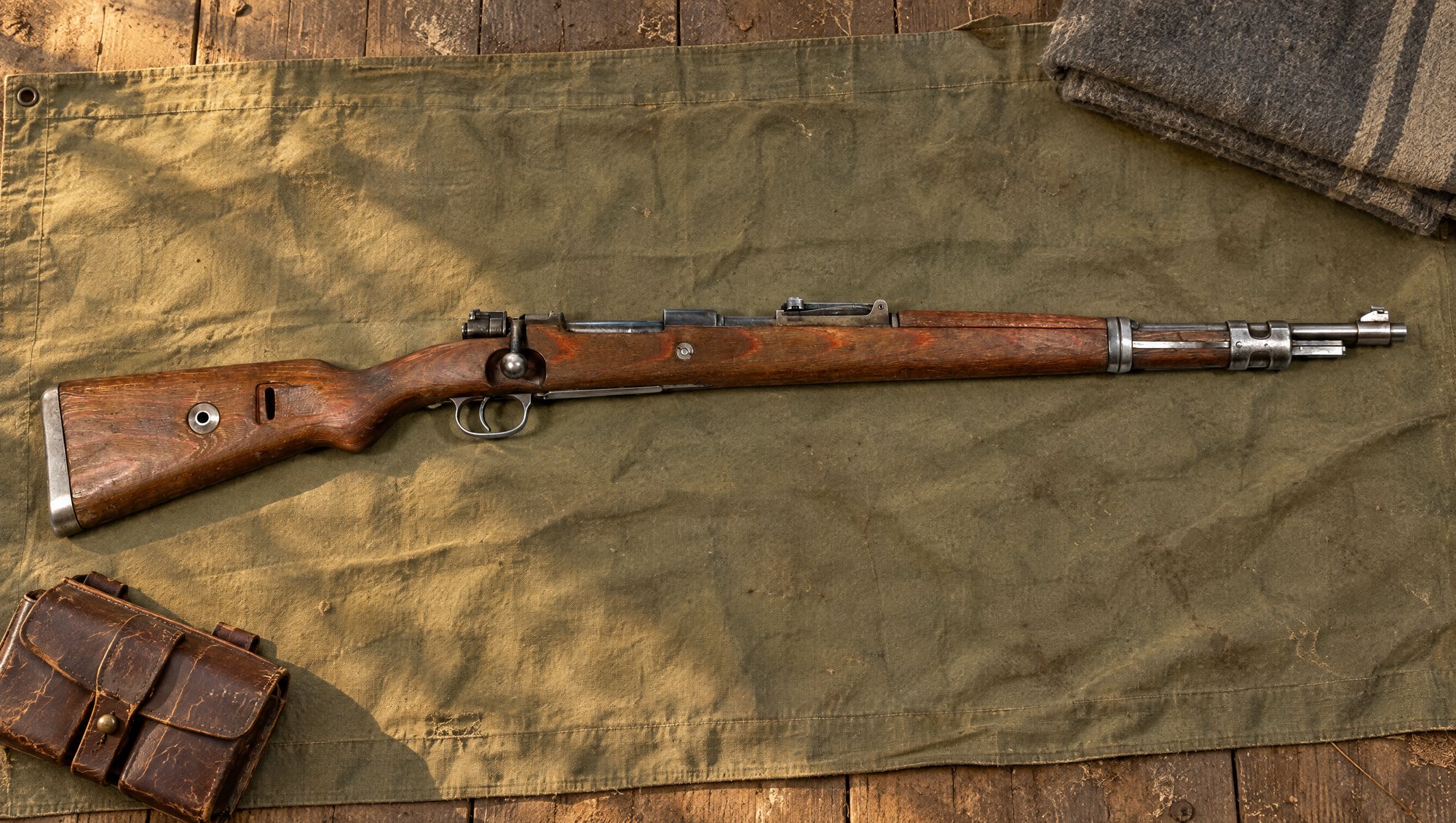 Karabiner 98k rifle with laminated stock lying on olive canvas beside a leather ammunition pouch